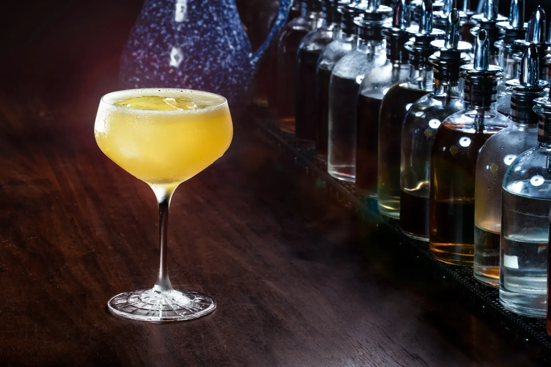 A golden sour in a coupe on the Dead Rabbit bar, dasher bottles racked along the back.
