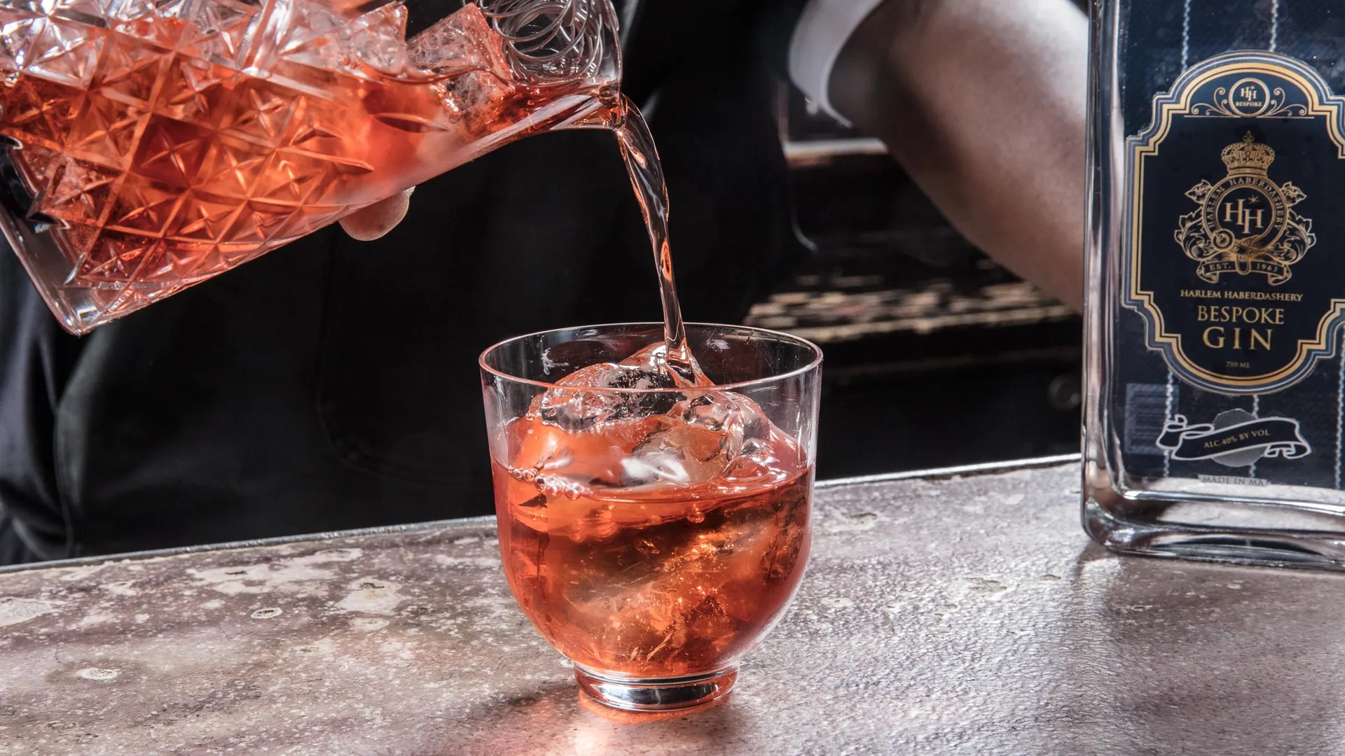 Negroni poured from a cut crystal mixing glass over ice, an HH Bespoke gin bottle standing on the bar beside it.