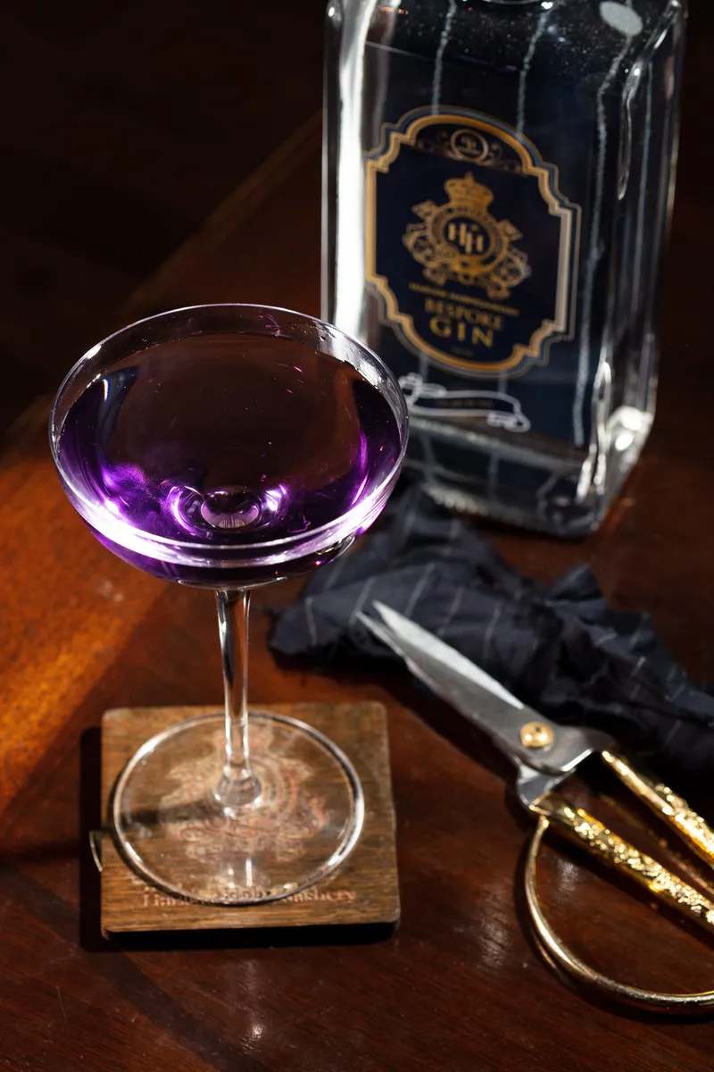 HH Bespoke gin bottle behind a violet cocktail in a coupe, brass scissors on the bar