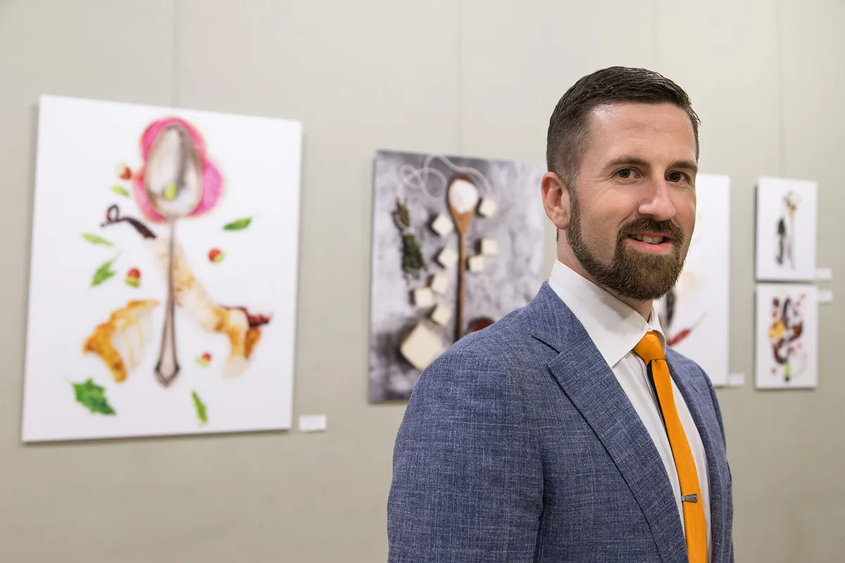 Brent Herrig in a blue linen jacket and orange tie at an exhibition of his Spoonfuls of Inspiration photographs.