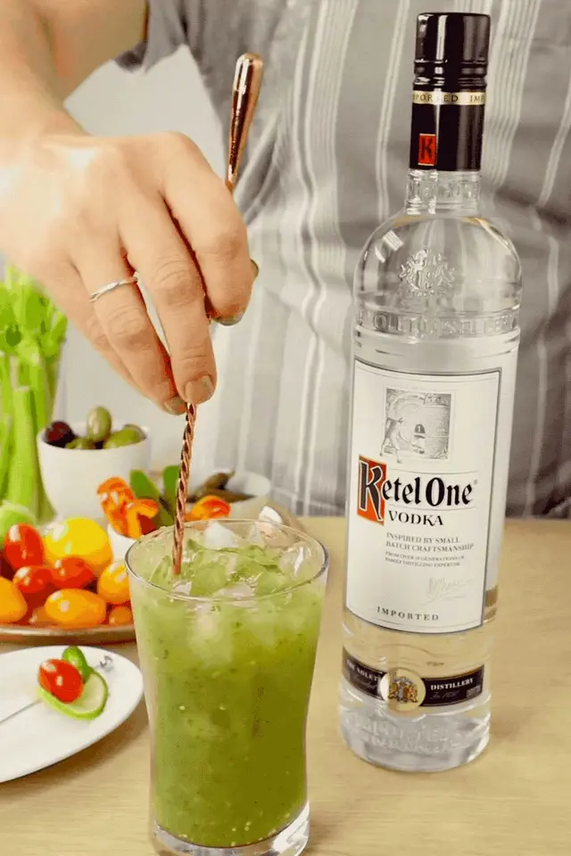 A hand stirs a green cocktail beside a Ketel One bottle, frame from a directed tabletop loop.